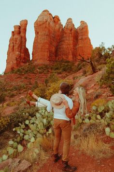 a man carrying a woman on his back while standing in front of some red rocks