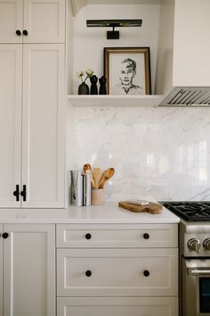 a kitchen with white cabinets and marble counter tops, an oven and stove top in the background