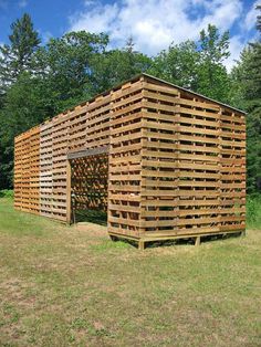 a large wooden structure sitting in the middle of a grass covered field next to trees