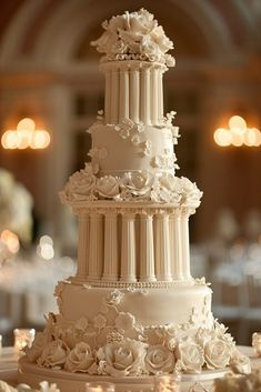 a three tiered white wedding cake with flowers on it's side and candles in the background