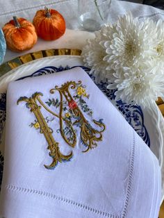 an embroidered monogram on a napkin next to flowers and pumpkins