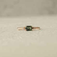 a green and white diamond ring sitting on top of a table next to a wall