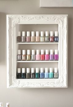 a white shelf filled with bottles of nail polish on top of a table next to framed pictures