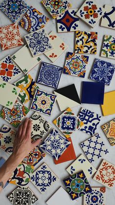 many different colored and patterned tiles are on the floor with one hand pointing at them