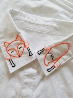 an embroidered fox on a white shirt with orange stitching around the collar and chest