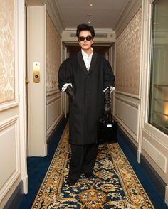 a man in a black coat and sunglasses is walking down the hallway