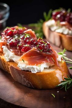 two pieces of bread with cream cheese and cranberry toppings on top, sitting on a wooden cutting board