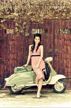 a woman standing next to a scooter in front of a wooden wall with vines