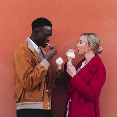 two people standing next to each other eating ice cream