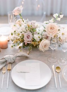 the table is set with white and pink flowers, silverware, and napkins