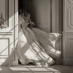 a woman in a long white dress is coming out of an open door with her back to the camera