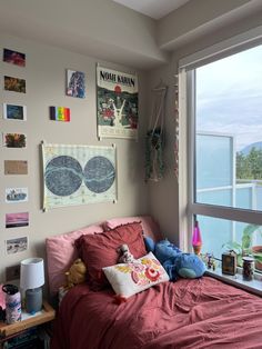 a bedroom with a large window and lots of pictures on the wall above it, along with a bed covered in red sheets