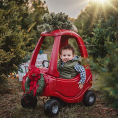 a little boy sitting in a red toy car with christmas wreaths on the front