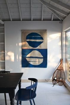 a room with a table, chairs and a painting on the wall above it that has a blue chair in front of it