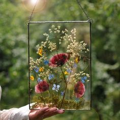 a person holding up a glass frame with flowers in it