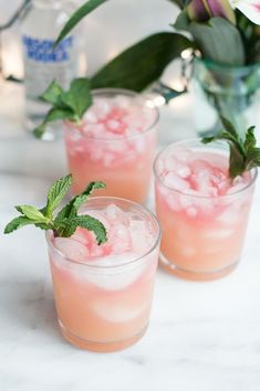 three glasses filled with ice and mint garnish sitting on a counter top next to flowers