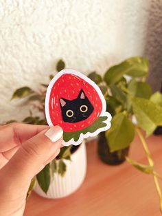 a hand holding up a sticker with a black cat on it's face