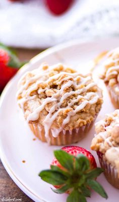 strawberry muffins with icing on a plate next to strawberries and leaves