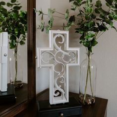 a white cross sitting on top of a wooden table next to a vase filled with flowers