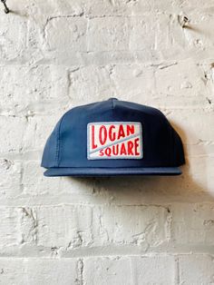 "Vintage Logan Square Hat  - (New) Cotton Unstructured 5 Panel Snapback in Navy Closure - 7 Button Plastic Snapf Color - Navy Construction - 5 Panel Snapback Contents - 60% Cotton / 40% Polyester Profile - 3.25\" Size - One Size Fits All (6 ⅝\" - 7 ⅝\") Structure - Lightly Structured - Logan Square Patch (Felt patch with embroidered lettering)" 7 Panel Hat, Vintage Everyday Short Brim Hat, Vintage 5-panel Hat For Everyday, Vintage Hat With Logo Patch And Flat Brim, Vintage Hat With Logo Patch Flat Brim, Vintage Flat Brim Hat With Logo Patch, Retro Hat With Flat Bill And Logo Patch, Everyday Trucker Hat With Short Brim, Retro Flat Bill Hat With Logo Patch