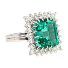 GIA Certified 8.17 Carat Tourmaline and Diamond Halo Square Shaped Ring in Platinum. This classy and sparkling ring has a center stone of tourmaline in a dazzling green color that has a blueish hue. The center stone has incredible luster and transparency that's unmatched. The emerald octagonal cut tourmaline is surrounded by 24 round-cut, prong-set diamonds with intricate detailing on the back of the stones and on the ring shank. Total weight is 9.31 grams.  Item Details: Item Type: Ring Metal: Platinum  Gemstones: Tourmaline; Diamonds Total Carats: 9.37 Weight: 7.66 Grams Ring Size: 6.5 (adjustable)   Main Gemstone Details: Type: Tourmaline Carats: 8.17 Shape: Octagonal Cutting Style: Step Cut Transparency: Transparent Color: Bluish Green Measurements: 11.86 x 10.90 x 7.87 mm Setting: Pro Gia Certified Green Sapphire Ring For Formal Occasions, Formal Gia Certified Green Sapphire Ring, Green Sapphire Ring With Halo Setting For Formal Events, Green Sapphire Ring With Halo Setting For Formal Occasions, Green Sapphire Ring With Brilliant Cut For Formal Occasions, Formal Green Sapphire Ring With Brilliant Cut, Green Brilliant Cut Sapphire Ring For Formal Occasions, Formal Emerald Cut Green Topaz Ring, Formal Green Sapphire Ring With Center Stone