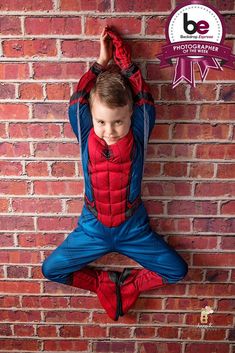 a young boy is sitting on the ground in front of a brick wall wearing a spiderman costume