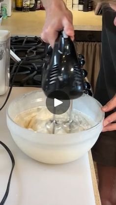 a person pouring batter into a bowl on top of a counter next to a blender