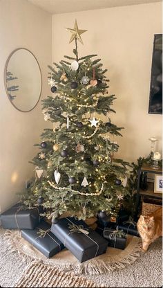 a christmas tree with presents under it and a cat sitting on the floor next to it