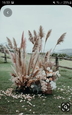 an arrangement of flowers and feathers in a basket on the grass near a wooden fence