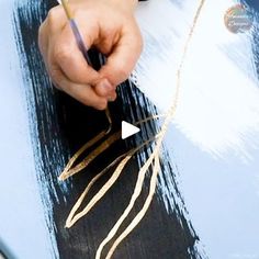 a person holding a pen and writing on a piece of paper with gold thread attached to it