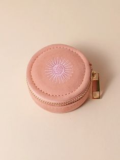 a pink round box with a gold chain around the bottom and an embroidered sun on it