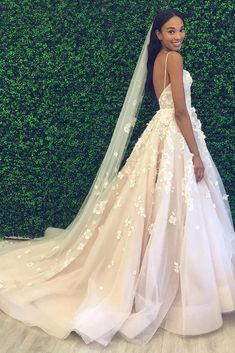 a woman standing in front of a green wall wearing a wedding dress with flowers on it