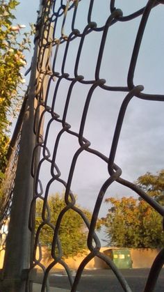 a close up view of a chain link fence with trees in the backgroud