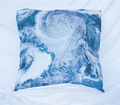 a blue and white pillow sitting on top of a white bed covered in pillows with swirls