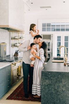 a man and woman holding two children in their arms while standing next to a kitchen counter