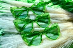 four green heart shaped glasses sitting on top of some white fur with leaves in the background