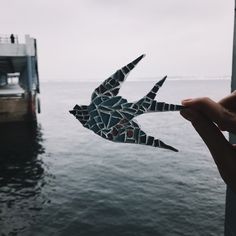 a hand holding up a piece of paper that looks like a bird flying over the water