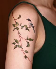 a woman's arm with a bird and green leaves on it