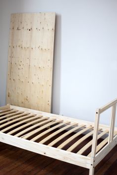 a wooden bed frame with slats on the bottom and sides, against a white wall