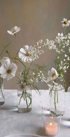 three vases filled with white flowers on top of a table next to a candle