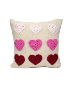 a crocheted pillow with pink and red heart appliques on the front