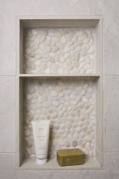 a white shelf with some soap and a gold box on it in front of a stone wall