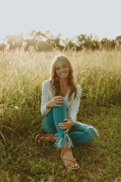 a woman sitting in the grass with her legs crossed and smiling at the camera,