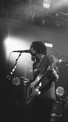 a man with dreadlocks playing guitar in front of a microphone and other musicians