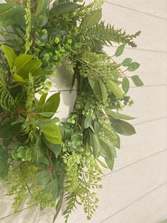 a green wreath hanging on the side of a white building with leaves and flowers around it