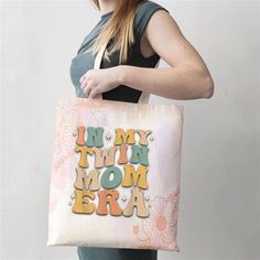 a woman holding a tote bag with the words in my twin mom era on it