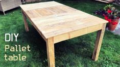 a table made out of pallet wood sitting in the grass next to a potted plant