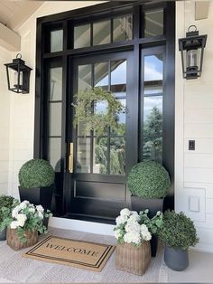 two potted plants are sitting on the front step of a house with a welcome mat