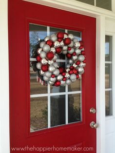 a red front door with a christmas wreath on it and ornaments hanging from the side