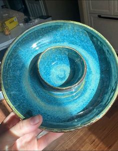 a hand holding a blue bowl on top of a wooden table